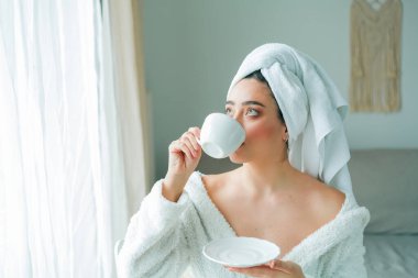 Duştan sonra, kafasında havlu olan bornozlu genç bir kadın kahve içer ve pencereden dışarı bakar. - Günaydın. Kahvaltı..