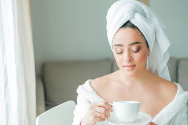 Duştan sonra, kafasında havlu olan bornozlu genç bir kadın kahve içer ve pencereden dışarı bakar. - Günaydın. Kahvaltı..