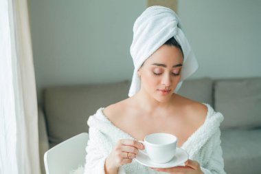 Duştan sonra, kafasında havlu olan bornozlu genç bir kadın kahve içer ve pencereden dışarı bakar. - Günaydın. Kahvaltı..