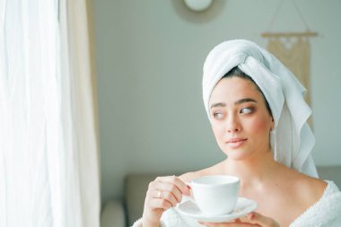 Duştan sonra, kafasında havlu olan bornozlu genç bir kadın kahve içer ve pencereden dışarı bakar. - Günaydın. Kahvaltı..