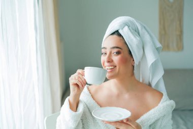 Duştan sonra, kafasında havlu olan bornozlu genç bir kadın kahve içer ve pencereden dışarı bakar. - Günaydın. Kahvaltı..