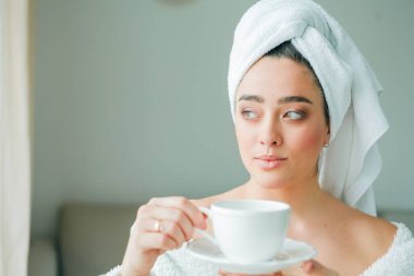 Duştan sonra, kafasında havlu olan bornozlu genç bir kadın kahve içer ve pencereden dışarı bakar. - Günaydın. Kahvaltı..