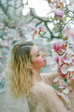 Çiçek açan bir manolya ağacının yanında genç ve güzel bir sarışın. Bahar. Yaz.
