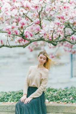 Çiçek açan bir manolya ağacının yanında genç ve güzel bir sarışın. Bahar. Yaz.