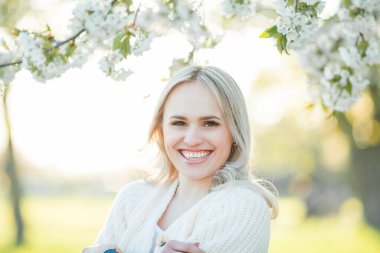 Güzel genç bir kadın çiçek açan bir bahçede piknikte dinleniyor. Beyaz çiçekler. Bahar.