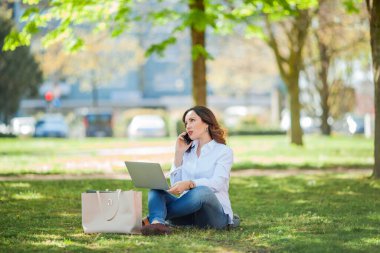 Genç mutlu kadın doğada bir dizüstü bilgisayarda çalışıyor. Karantinaya alın. Serbest çalışan biri. Şehir.