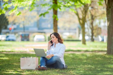 Genç mutlu kadın doğada bir dizüstü bilgisayarda çalışıyor. Karantinaya alın. Serbest çalışan biri. Şehir.