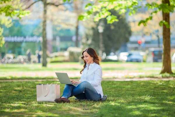 Young happy woman works at a laptop in nature. Quarantine. Freelancer. City.