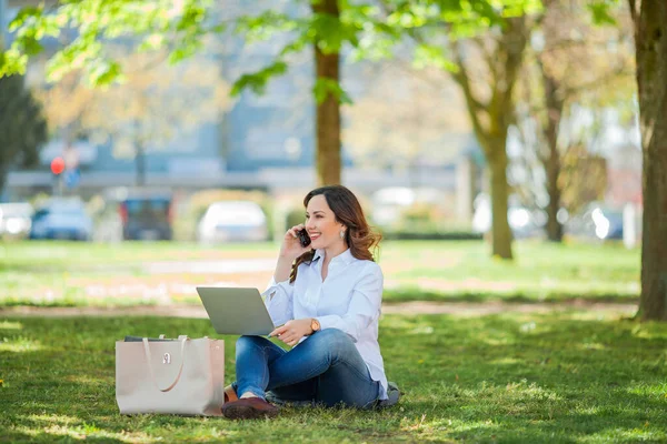 Young happy woman works at a laptop in nature. Quarantine. Freelancer. City.