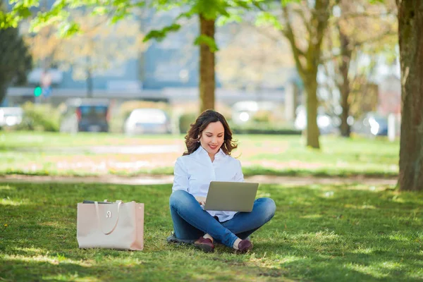 Young happy woman works at a laptop in nature. Quarantine. Freelancer. City.