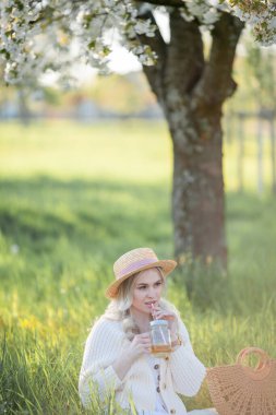 Güzel genç bir kadın çiçek açan bir bahçede piknikte dinleniyor. Beyaz çiçekler. Bahar.