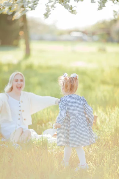 一位漂亮的年轻母亲和她的小女儿正在花园子里野餐 白色的花春天 — 图库照片
