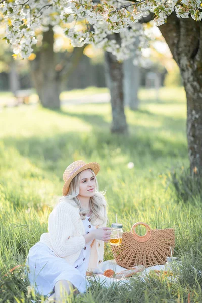 美しい若い女性が咲く庭のピクニックに休んでいます 白い花 — ストック写真