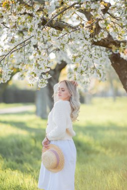 Güzel genç bir kadın çiçek açan bir bahçede piknikte dinleniyor. Beyaz çiçekler. Bahar.