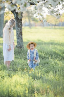 Güzel genç bir anne ve küçük kızı çiçek bahçesindeki bir piknikte dinleniyorlar. Beyaz çiçekler. Bahar.