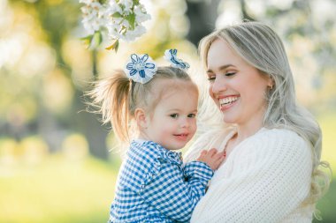 Güzel genç bir anne ve küçük kızı çiçek bahçesindeki bir piknikte dinleniyorlar. Beyaz çiçekler. Bahar.