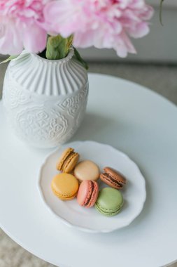 Oturma odasının içi. Vazoda bir buket pembe şakayık, rengarenk Fransız kurabiyesi. Samimi.