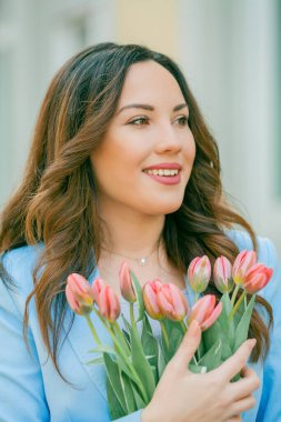 Mavi takım elbiseli, bir buket lale taşıyan güzel bir genç kadının portresi..