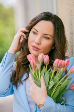 Mavi takım elbiseli, bir buket lale taşıyan güzel bir genç kadının portresi..
