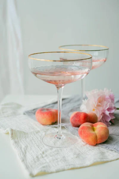 Beautiful glass with pink champagne, peaches on the background. Peonies.