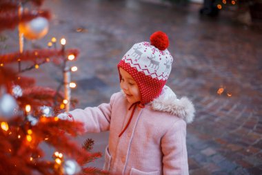 Bir Avrupa şehrinin caddesindeki Noel ağacının yanında şapkalı ve eldivenli küçük şirin bir kız. Tatiller.