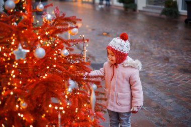 Bir Avrupa şehrinin caddesindeki Noel ağacının yanında şapkalı ve eldivenli küçük şirin bir kız. Tatiller.