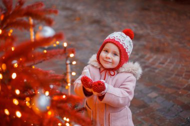 Bir Avrupa şehrinin caddesindeki Noel ağacının yanında şapkalı ve eldivenli küçük şirin bir kız. Tatiller.