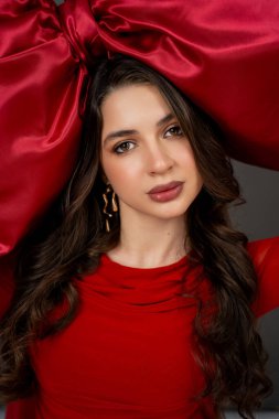 Yeni yıl konsepti. Elinde büyük kırmızı bir fiyonk olan, şenlikli elbiseli genç bir kadının portresi. Noel.