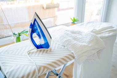 Elektrikli ütü, pencerenin yanındaki ütü masasında yeni yıkanmış giysiler. Ev.