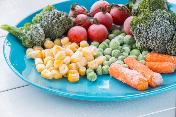 Legumes congelados brócolis, tomate cereja, milho, ervilha, cenoura em prato azul Imagem De Stock