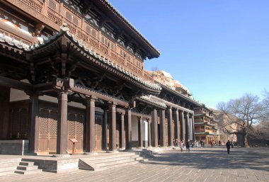 Çin 'in Shanxi Eyaleti, Datong yakınlarında Yungang Grottoes. Yungang Grottoes 'un ziyaretçilerle dış görünüşü. Ahşap binalar kayalıklara bağlı ve mağaraların önünü kaplıyorlar..
