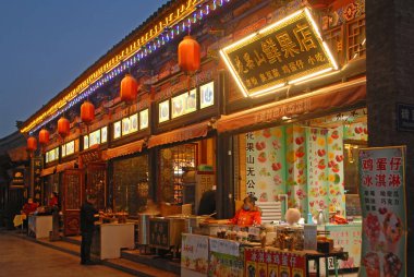 Pingyao, Shanxi Eyaleti, Çin. Gece Pingyao 'da şehir ışıkları ve kırmızı fenerlerle bir sokak sahnesi. Pingyao eski kasabasında restoranları ve mağazaları olan bir sokak, Çin 'in ünlü antik duvarlı bir şehri..