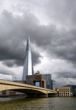 Londra, İngiltere: Londra şehrinden Londra Köprüsü ve Çömlek Binası ile Thames Nehri 'nin güneyine bakan görüntüler. Arkasında kara fırtına bulutlarıyla Çömlek 'e yansıyan ışık..