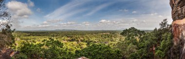 Beautiful panoramic view of the green valley at the foot of the Sigiriya cliff. The mountains in the background merge with the clouds. Sri Lanka.