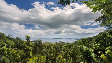 Tropikal ada. Tropikal bitki örtüsüyle kaplı dağlardan kıyıya ve yakındaki diğer adalara bakın. Beyaz bulutlu mavi gökyüzü. Seyşeller, Praslin Adası.