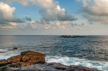 Gün batımında dalgalar kayaların üzerinde kırılır. Deniz yosunlarıyla kaplı kıyı kayası hâlâ güneş tarafından aydınlatılıyor. Sri Lanka.
