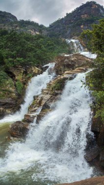 Sri Lanka dağlarındaki kayaların arasında şelale. Kayaların her iki tarafında da farklı yeşil bitkiler var..
