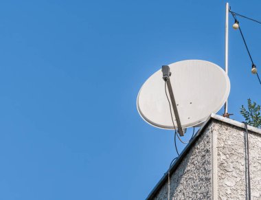 Mavi gökyüzüne karşı bir binanın çatısındaki uydu anteni ya da parabolik anten.