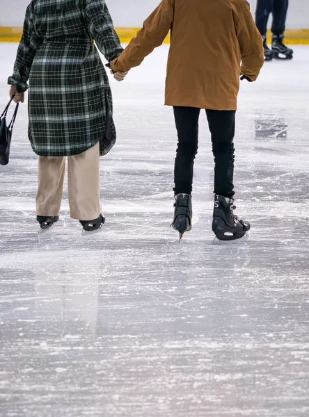 Two women with skates on ice holding hands. Ice skating recreational activity.