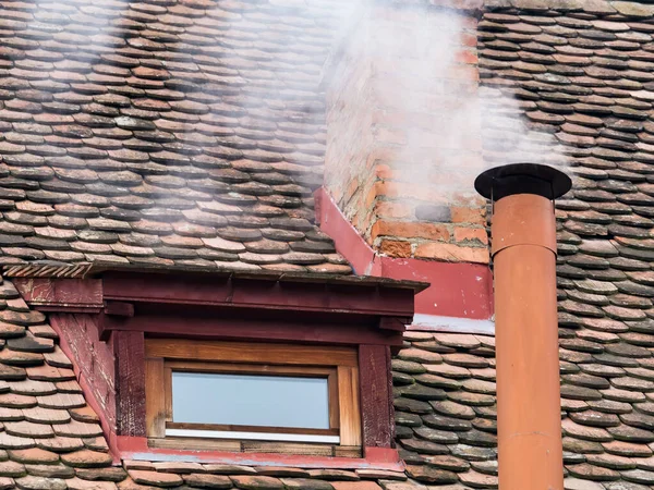 Kırsal alan, eski kırmızı kiremit çatılı bir evin bacasından yükselen dumanla birlikte.