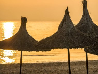 Karadeniz 'in sakin suları üzerinde güzel bir gün doğumu ya da gün batımı. Plaj yazı manzarası. Gün batımında ya da gün doğumunda kumsalda saman şemsiyesi