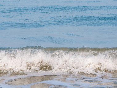 Small breaking waves with foam on the beach of the Black Sea.