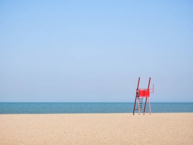 Boş bir sahilde kırmızı cankurtaran sandalyesi..