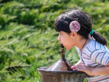 Bükreş, Romanya - 04.10.2021: Parktaki bir musluk veya çeşmeden su içen susamış genç kız.