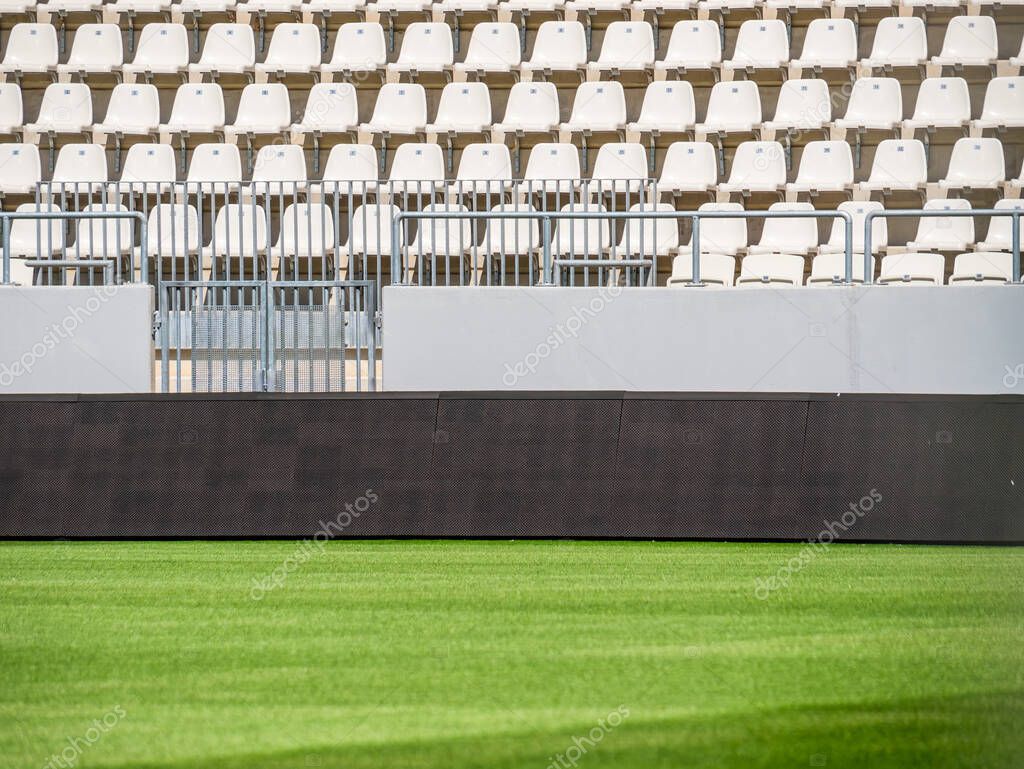 Empty stadium with white chairs in tribune and the green lawn grass