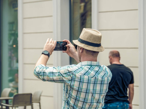 Hipster tourist wearing a hat taking pictures with a smartphone in Timisoara, Romania