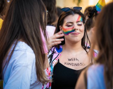 Bükreş, Romanya - 08.14.2021: Septum piercingli güzel bir kız ve LGBTQ Onur Yürüyüşü mitinginde yüzünde gökkuşağı bayrağı resmi .