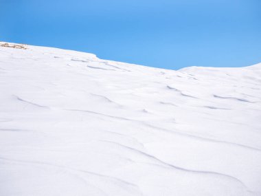 Açık mavi gökyüzüne karşı beyaz karla kaplı bir dağın ayrıntıları.