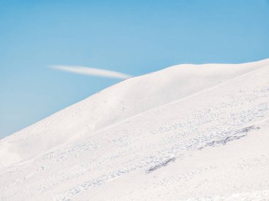 Açık mavi gökyüzüne karşı beyaz karla kaplı bir dağla ilgili detay. Patikadaki taze karda ayak sesleri