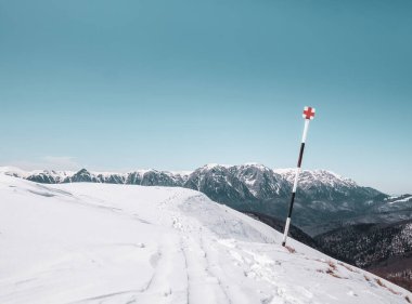 Arka planda dağ olan bir direğin üzerinde kızıl haç yürüyüş izleri var. Bucegi Dağları 'ndaki kış manzarası Romanya
